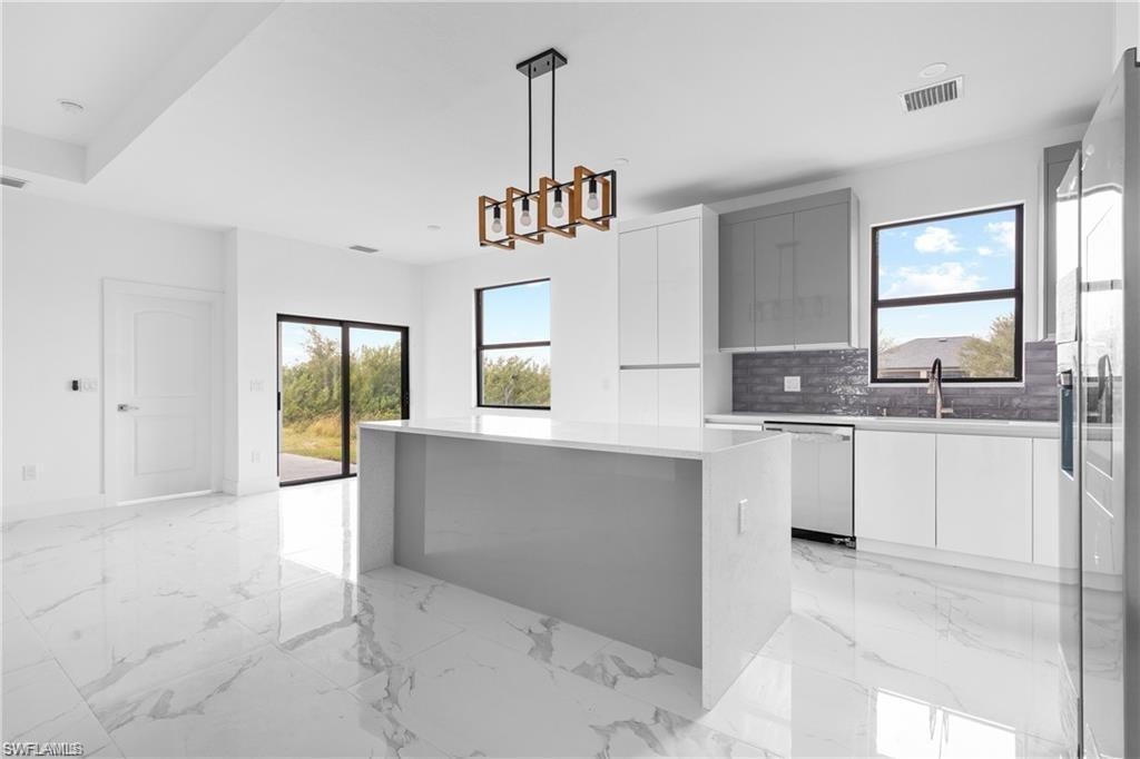 Modern kitchen featuring an extended island with a light-toned countertop, white and gray cabinetry, stainless steel appliances, and a gray tile backsplash