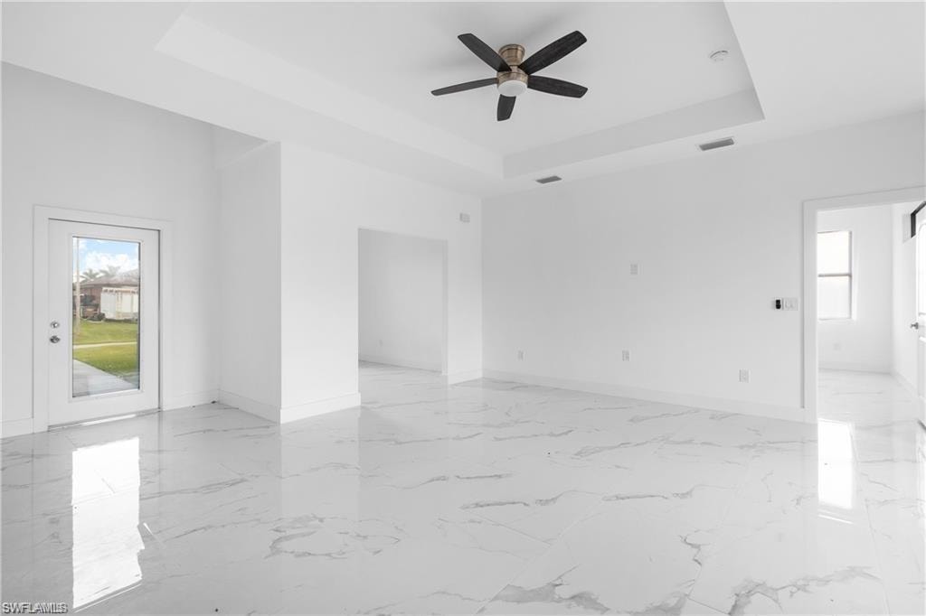 Spacious room featuring white tile flooring, tray ceiling, and a ceiling fan