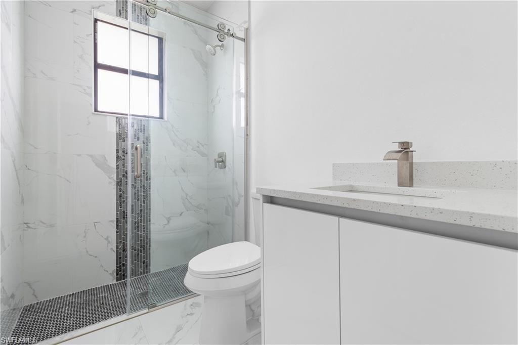 Modern bathroom featuring a frameless glass shower enclosure with a mosaic tile accent strip, a white vanity with an integrated sink, a speckled countertop, and brushed nickel fixtures
