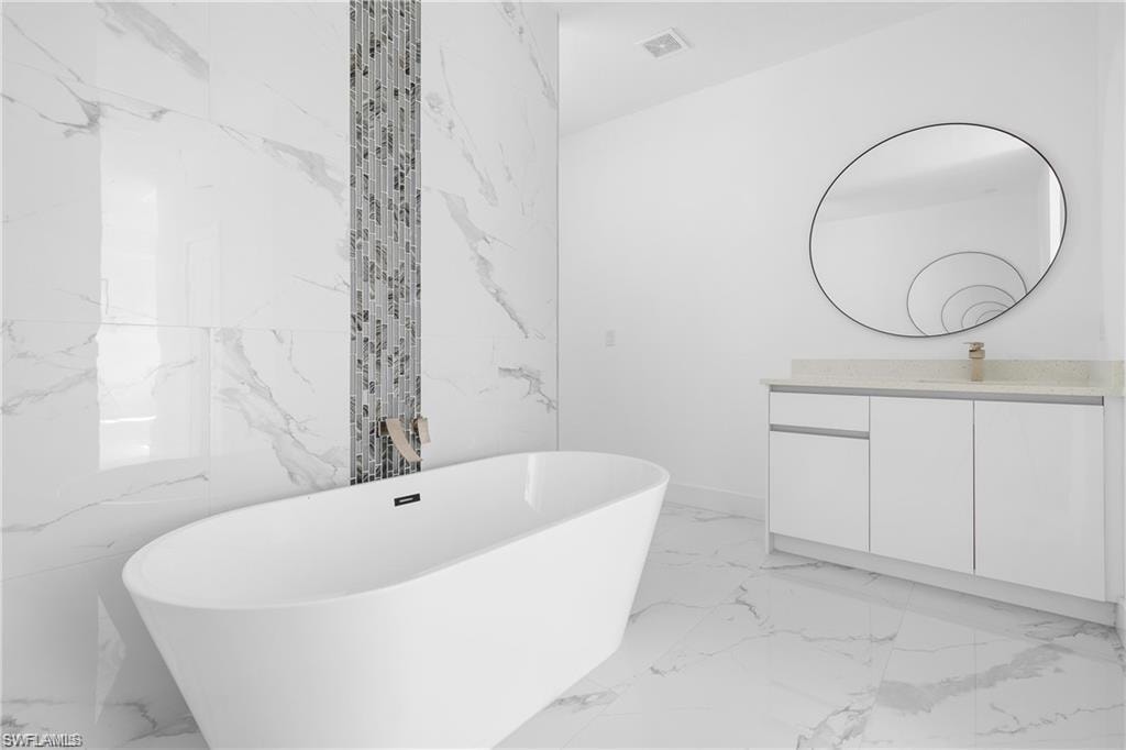 Freestanding soaking tub set against a feature wall with full-height marble-look tile and a vertical mosaic accent