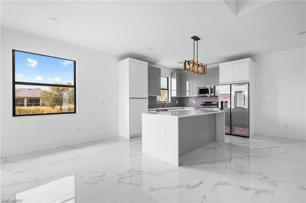 Open-concept kitchen featuring an oversized island, stainless steel appliances, contemporary pendant lighting, and white cabinetry