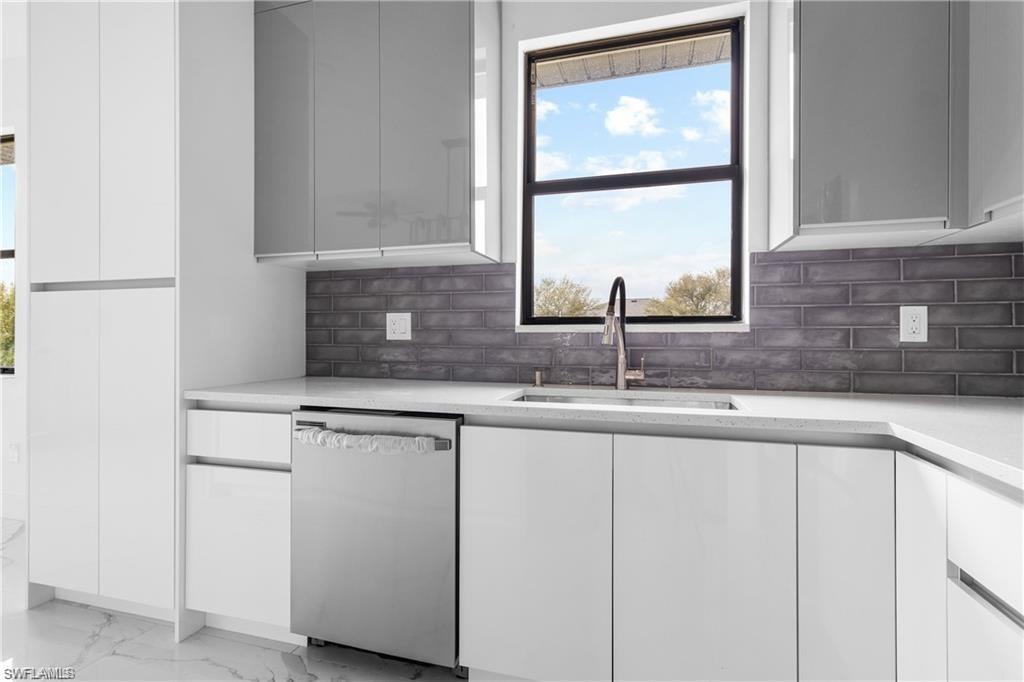 Modern kitchen featuring white cabinetry, a stainless steel dishwasher, and a window above the sink