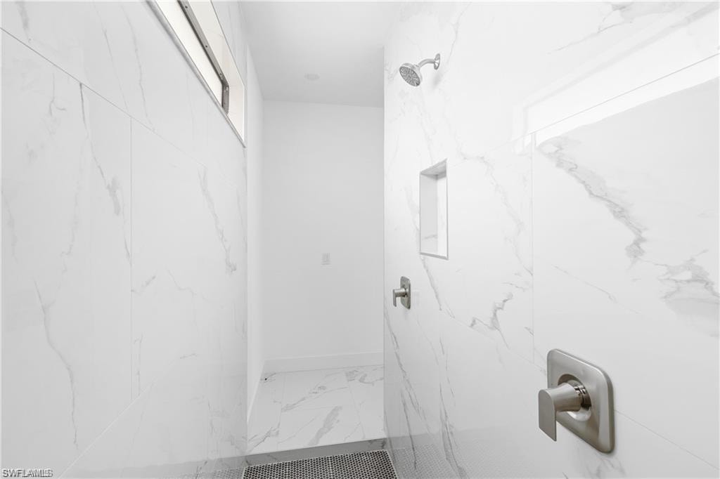 Walk-in shower featuring large format tile with subtle veining, brushed nickel fixtures, a built-in shower niche, and a linear window