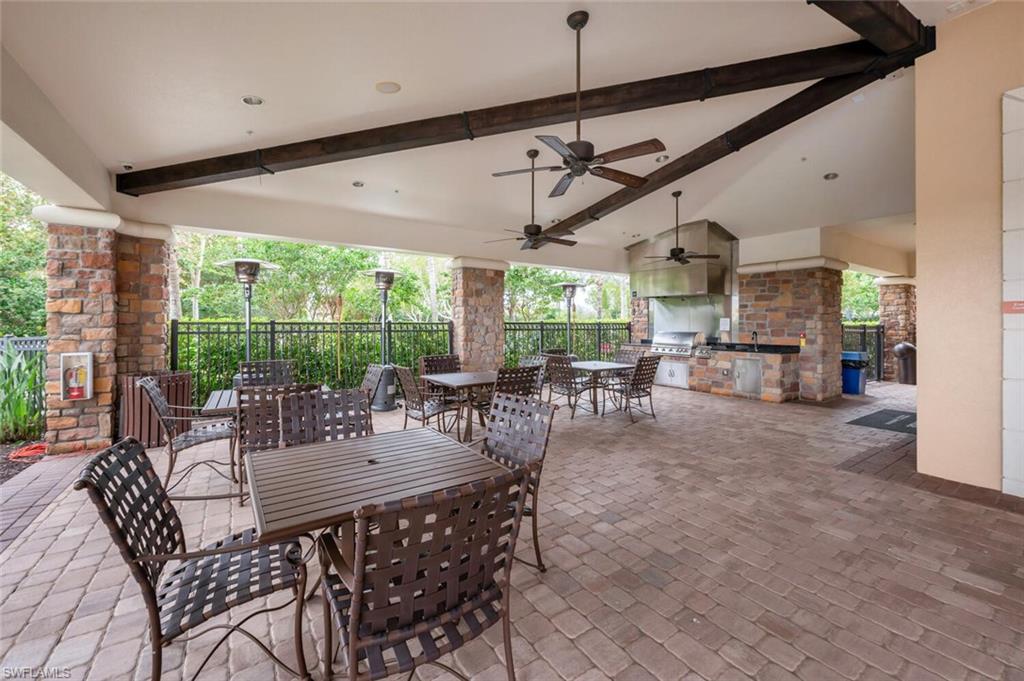 Covered outdoor patio featuring extensive paver flooring, stone column accents, and exposed wood-finish ceiling beams