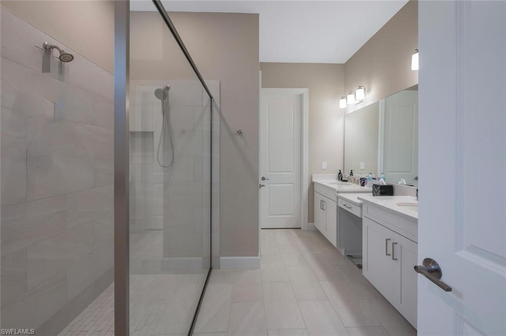 Spacious bathroom featuring a glass-enclosed shower, dual vanities with undermount sinks, and light-toned tile flooring