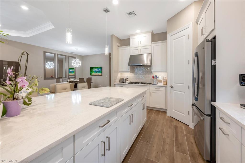 Kitchen featuring a large central island with light-toned countertops, white shaker cabinetry, stainless steel appliances, and wood-finish flooring