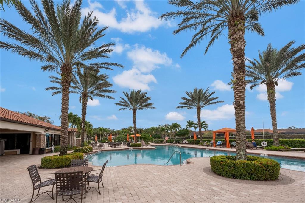 Resort-style pool area featuring a large swimming pool, paver deck, mature palm trees, and an open-air cabana