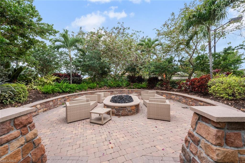 Stone fire pit area featuring a paver patio, a curved stone accent wall, and lush tropical landscaping