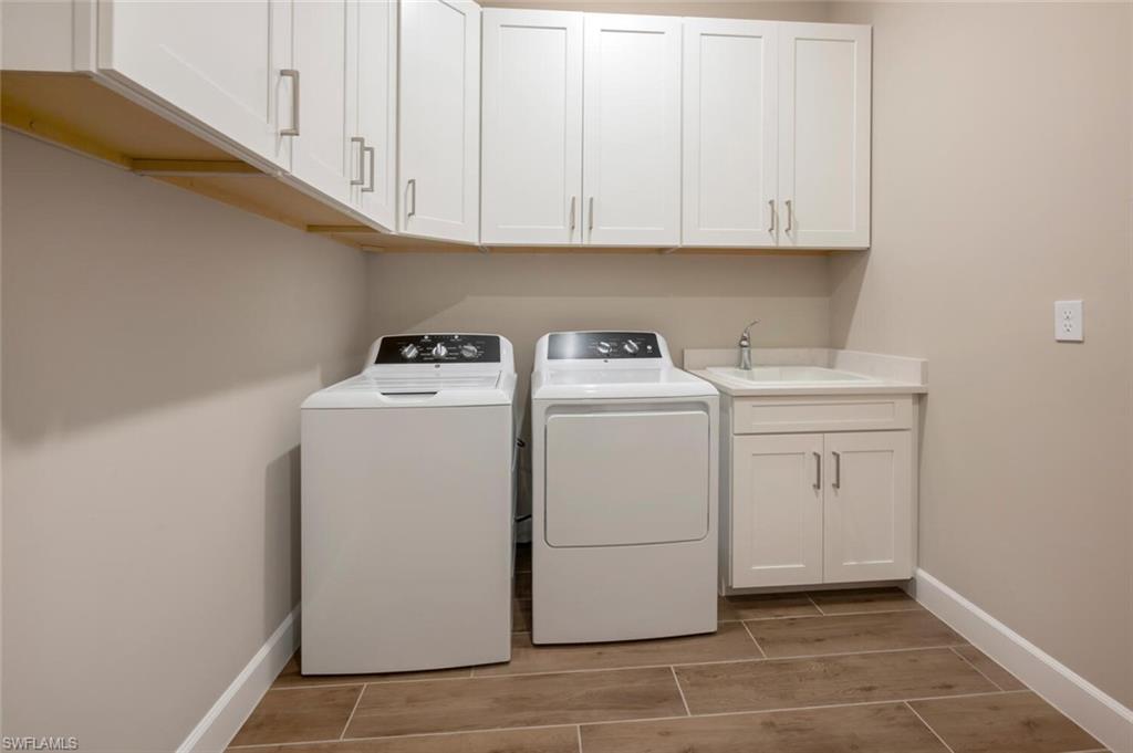 Dedicated laundry area featuring white shaker-style cabinetry with brushed nickel hardware, a utility sink with a chrome faucet, and wood-finish flooring