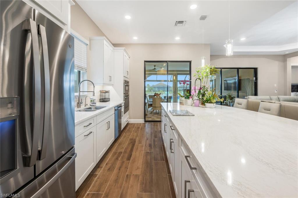 Modern kitchen featuring an expansive island with a light-toned countertop, white cabinetry with contemporary hardware, stainless steel appliances, and wood-finish flooring