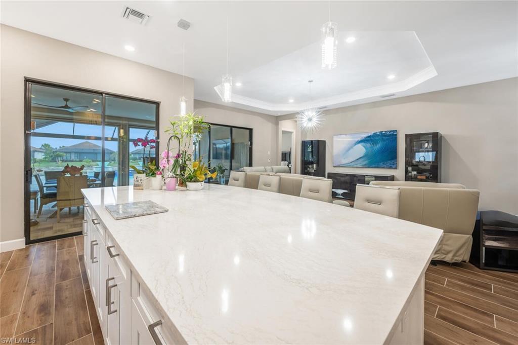 Spacious open-concept living area featuring an expansive kitchen island with a light-toned countertop, white cabinetry with contemporary pulls, wood-finish flooring, and a tray ceiling