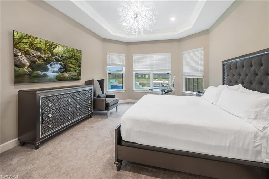 Recessed tray ceiling with a crystal chandelier, bay windows, and carpeted flooring