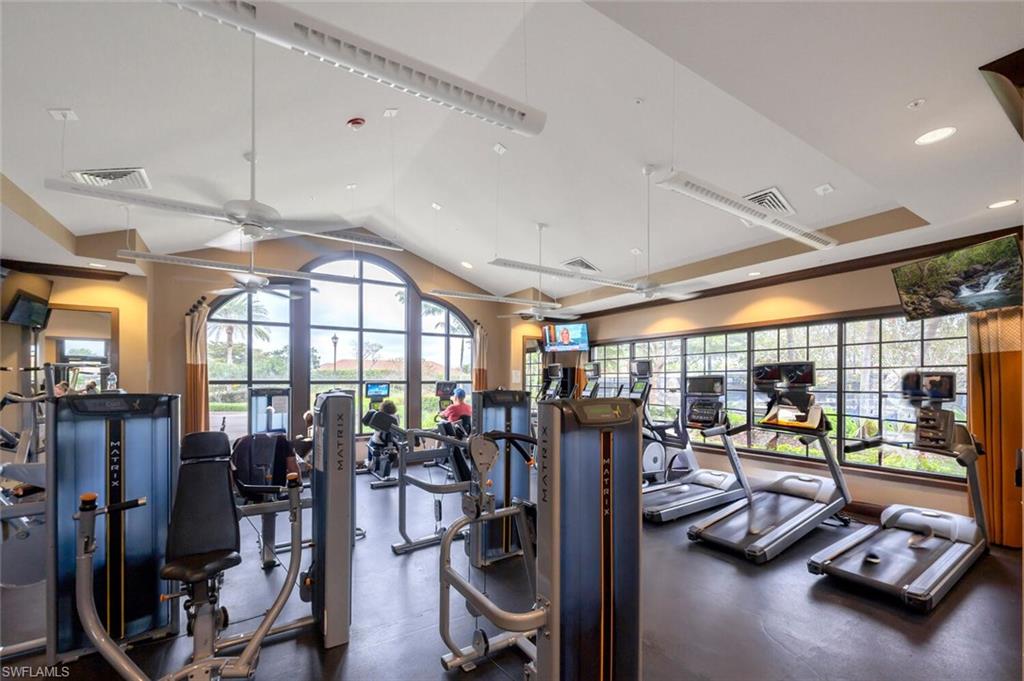 Fitness center featuring vaulted ceilings with exposed beams, arched transom windows, extensive exercise equipment, multiple wall-mounted televisions, and durable rubber flooring