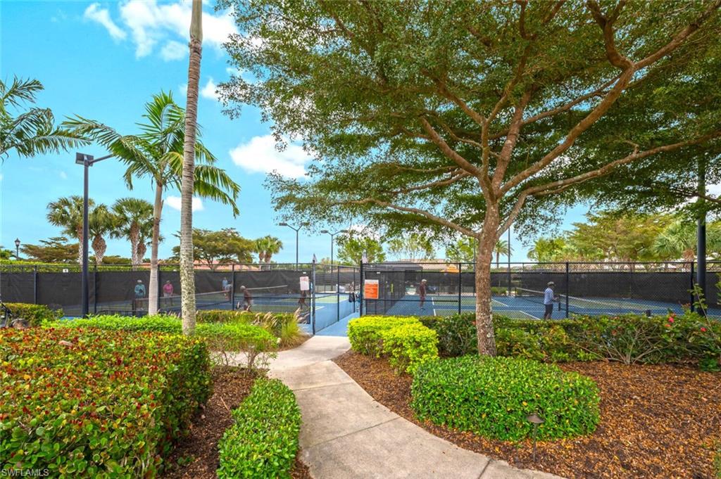Concrete pathway leading to multiple enclosed tennis courts with black fencing and surrounding landscape lighting