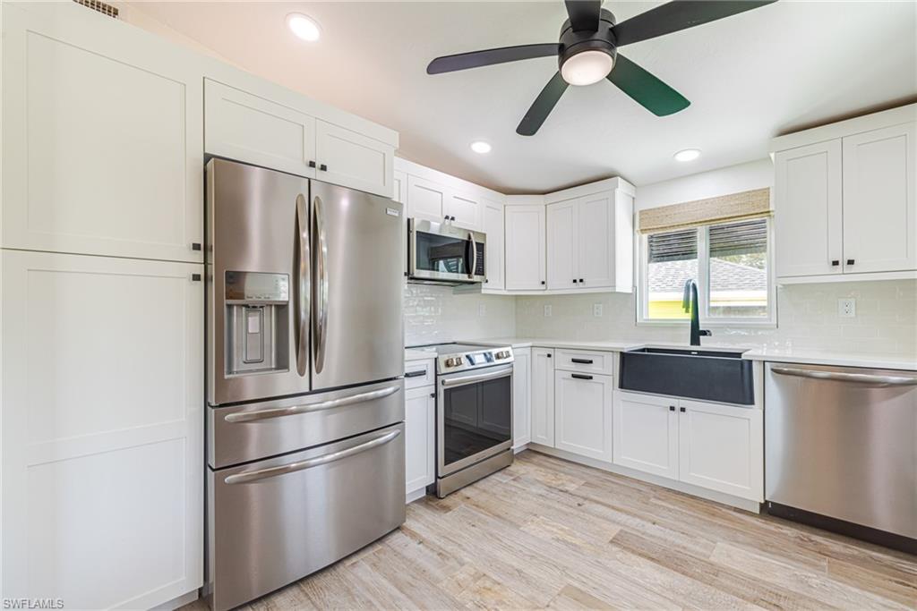 Modern kitchen featuring white shaker cabinetry, stainless steel appliances, wood-finish flooring, recessed lighting, and a black farmhouse sink with a matching faucet