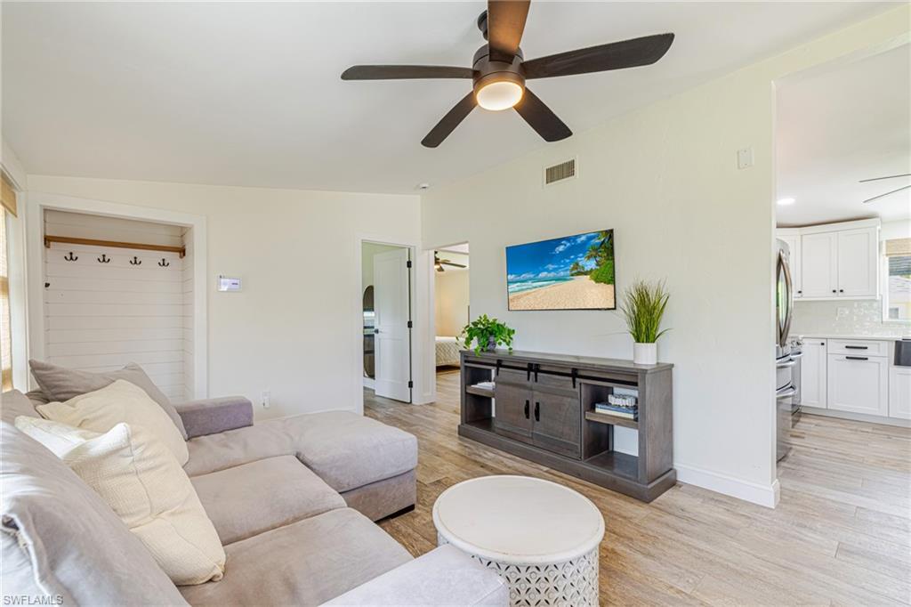 Spacious living area featuring wood-finish flooring, a contemporary ceiling fan with integrated lighting, and an open entryway to the kitchen