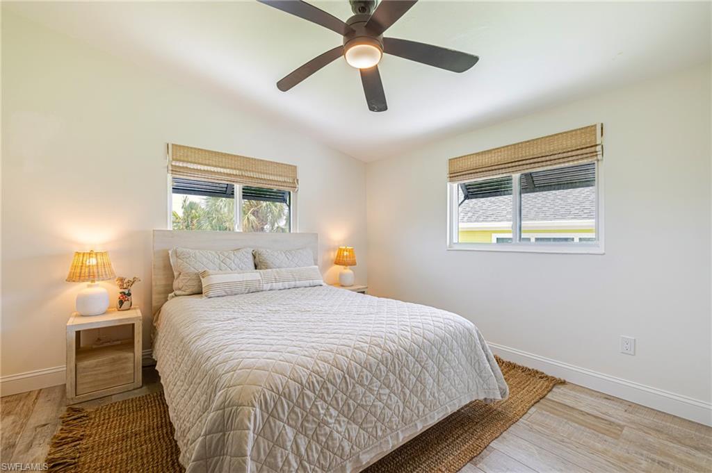 Bedroom featuring a ceiling fan with integrated lighting, wood-finish flooring, and white baseboards