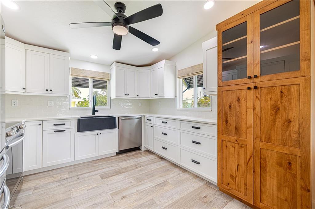 Well-appointed kitchen featuring light wood-finish flooring, white cabinetry with black hardware, and an integrated farmhouse sink