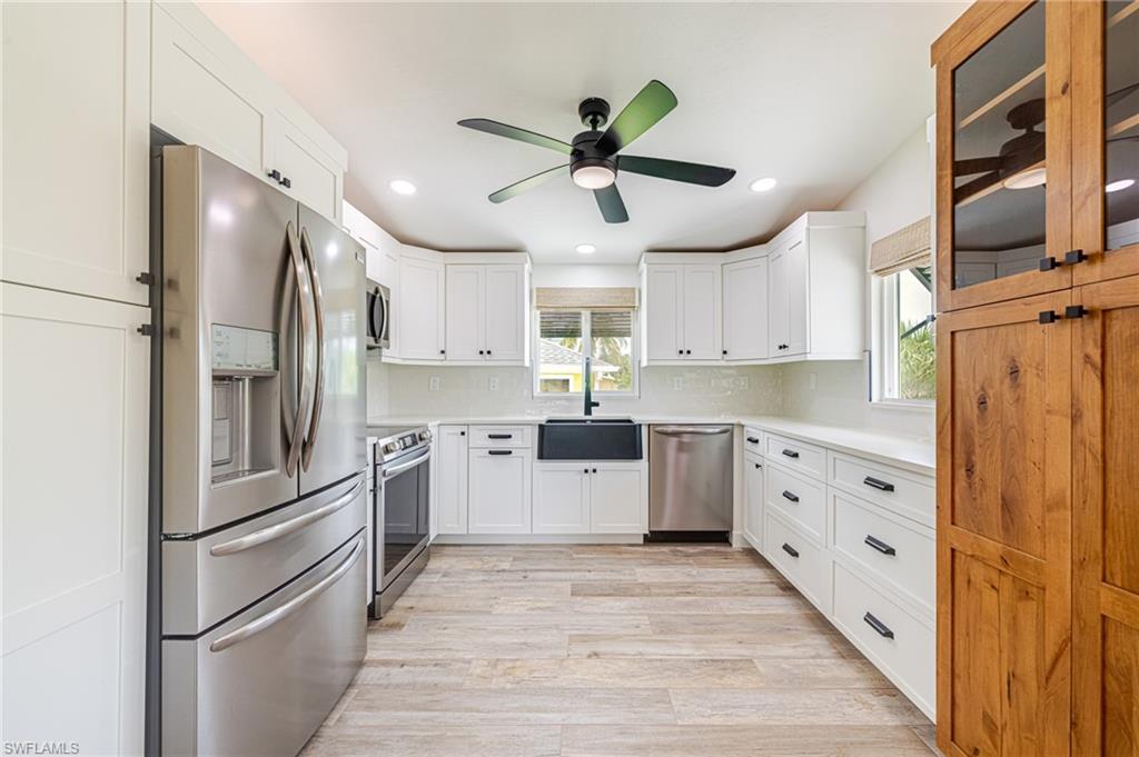 Renovated kitchen featuring wood-finish flooring, white shaker cabinetry, stainless steel appliances, and a black ceiling fan