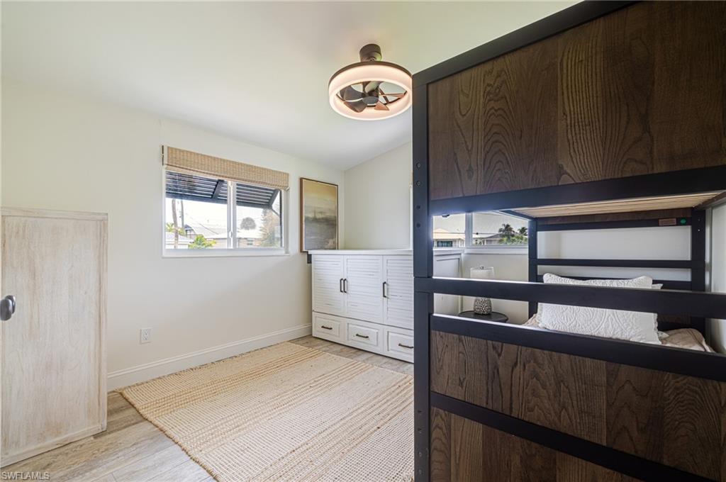 Bedroom featuring light wood-finish flooring, a white built-in storage unit with dark hardware, a window with a woven shade, and a ceiling fan with integrated lighting