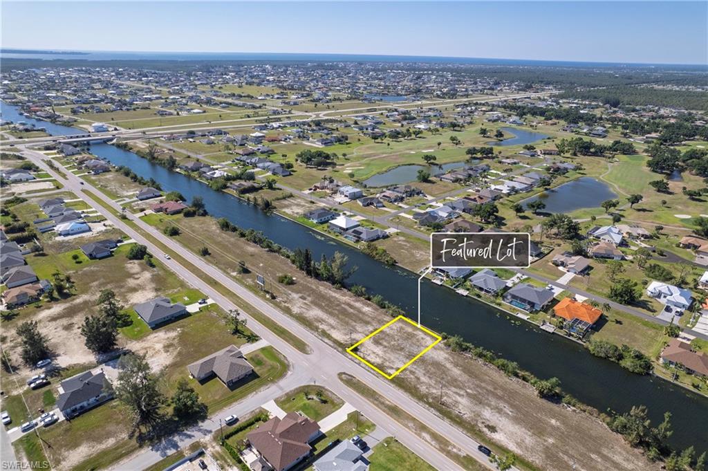 Canal-front lot featuring road access, surrounding residential properties, and proximity to golf course waters