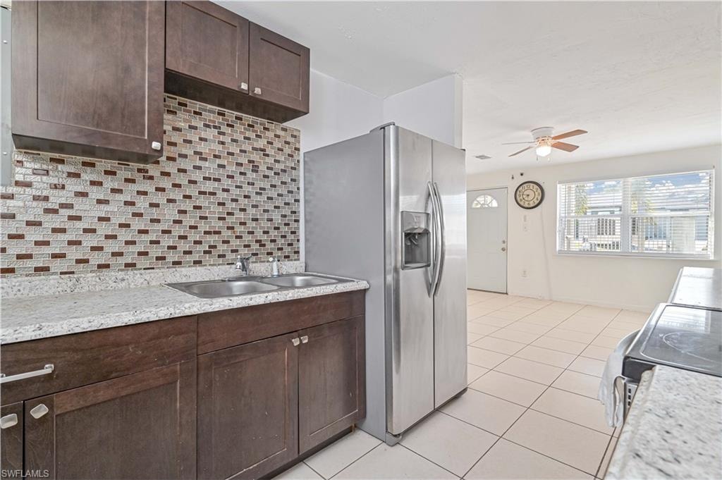 Kitchen with dark brown cabinetry, backsplash, appliances with stainless steel finishes, light tile patterned floors, and a ceiling fan