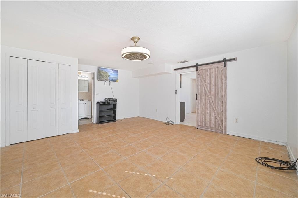 Unfurnished bedroom with a closet, a barn door, light tile patterned floors, and connected bathroom