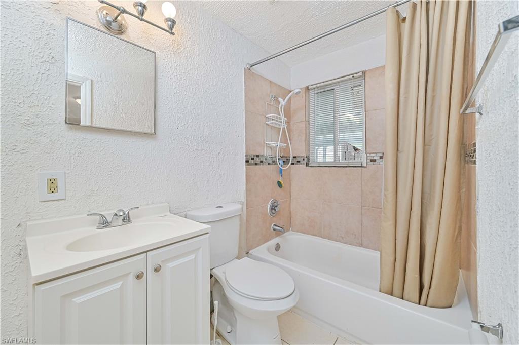 Full bathroom featuring a textured wall, shower / bath combo, a textured ceiling, and vanity