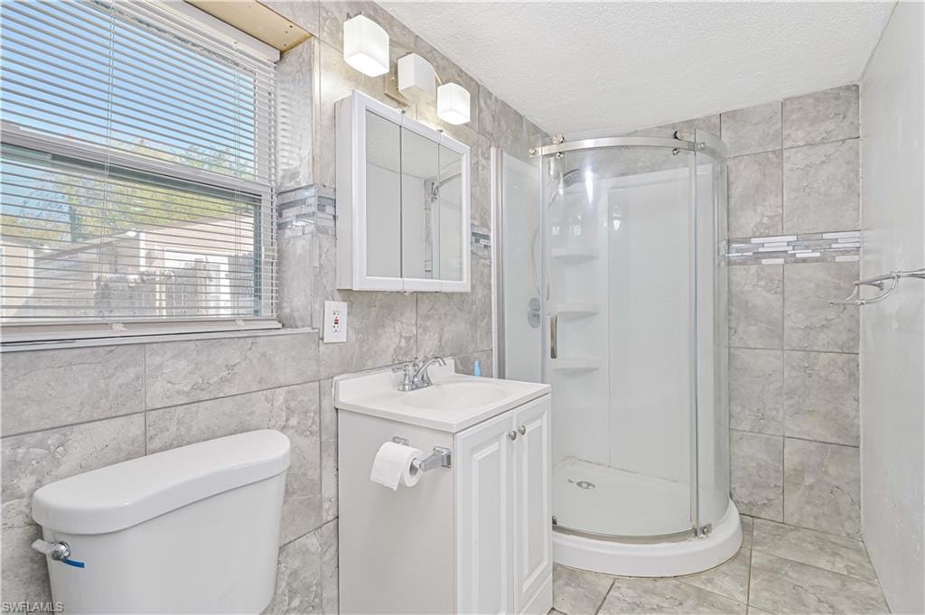 Bathroom with tile walls, a shower stall, a textured ceiling, and vanity
