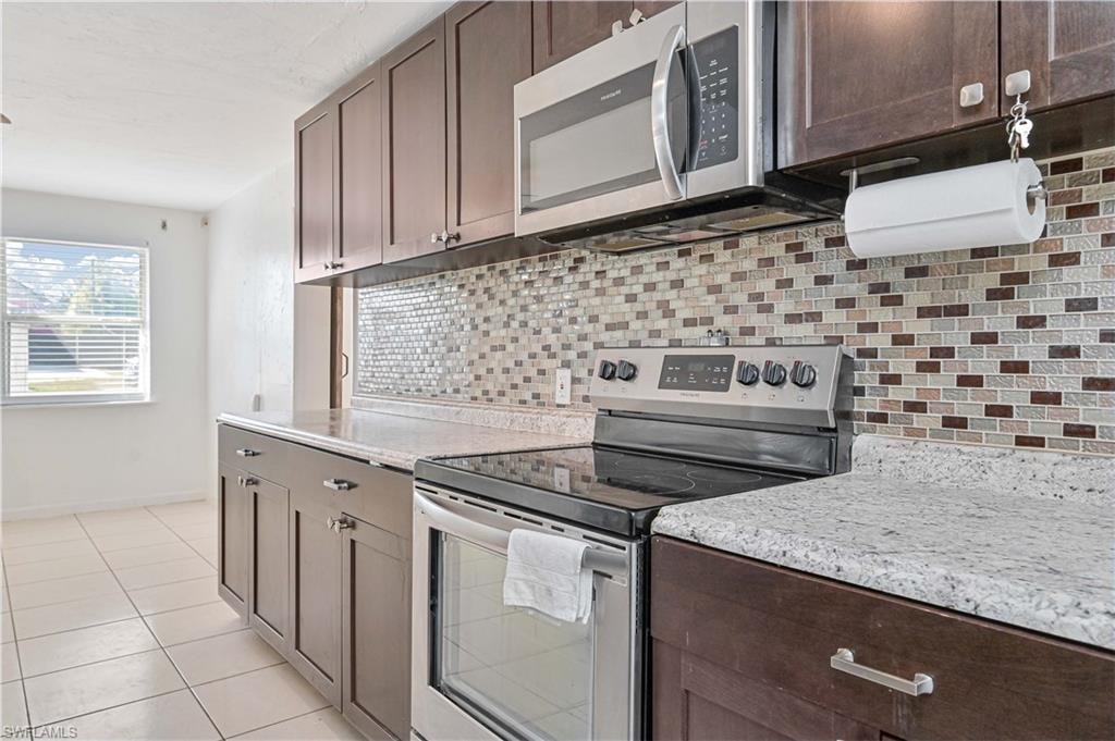 Kitchen with appliances with stainless steel finishes, dark brown cabinets, tasteful backsplash, and light tile patterned floors