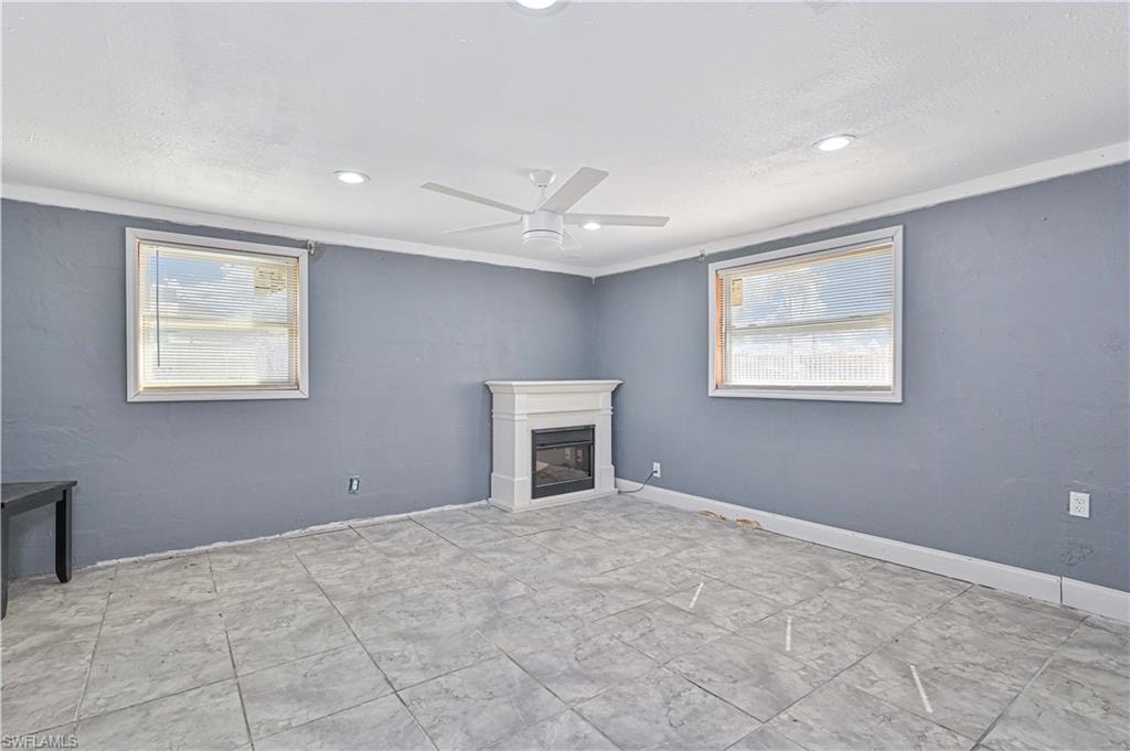 Unfurnished living room featuring a ceiling fan, a glass covered fireplace, and crown molding