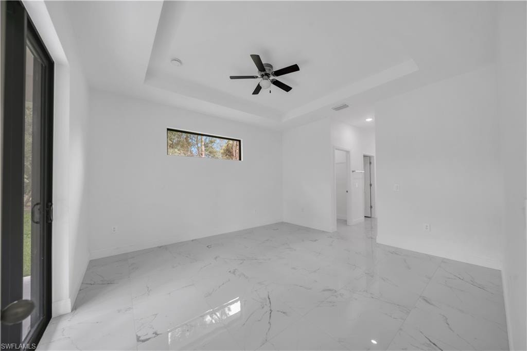 Spacious interior room featuring large format tile flooring, a tray ceiling, and a ceiling fan