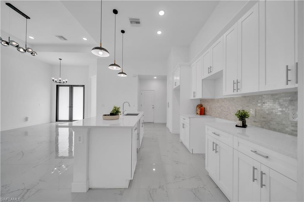 Contemporary kitchen featuring a large island with sink, white shaker cabinetry, light-toned countertops, and a mosaic tile backsplash