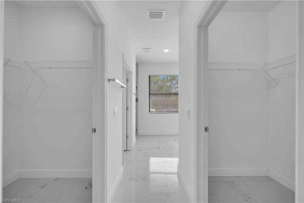 Hallway featuring two open closet spaces with wire shelving, light-toned tile flooring, white walls, and a window providing natural illumination