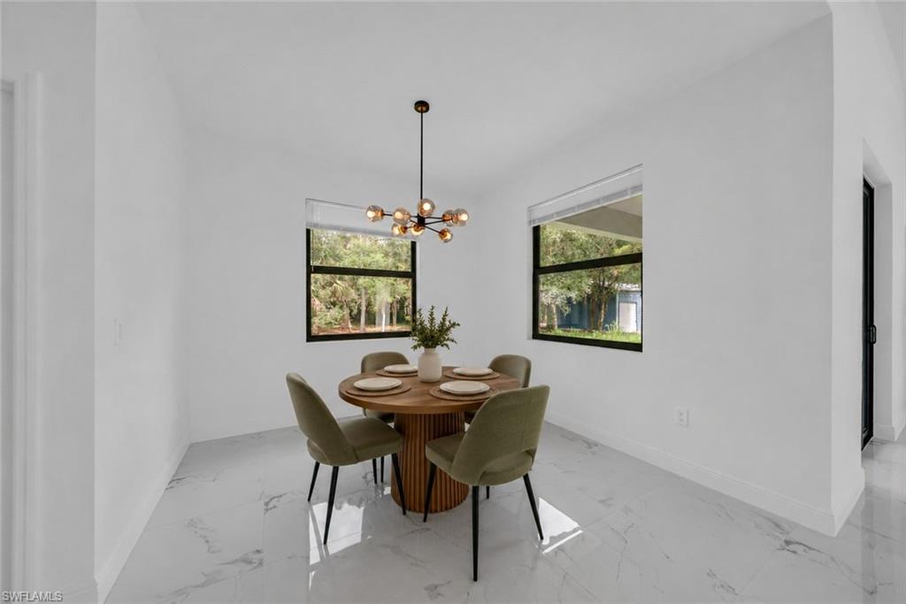 Dedicated dining room featuring a round wood-finish table, four upholstered chairs with metal legs, polished stone flooring with linear detailing, and dual black-framed windows flooding the space with natural light