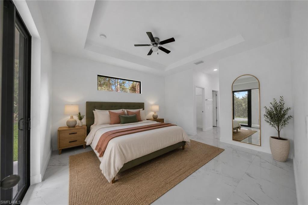 Spacious bedroom featuring white walls, a tray ceiling with a ceiling fan, and large format marble-look tile flooring