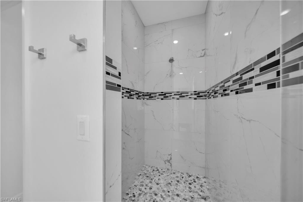 Spacious shower enclosure featuring large format white tile with subtle veining, dual mosaic tile accent bands, pebble-style shower floor, and a wall-mounted showerhead