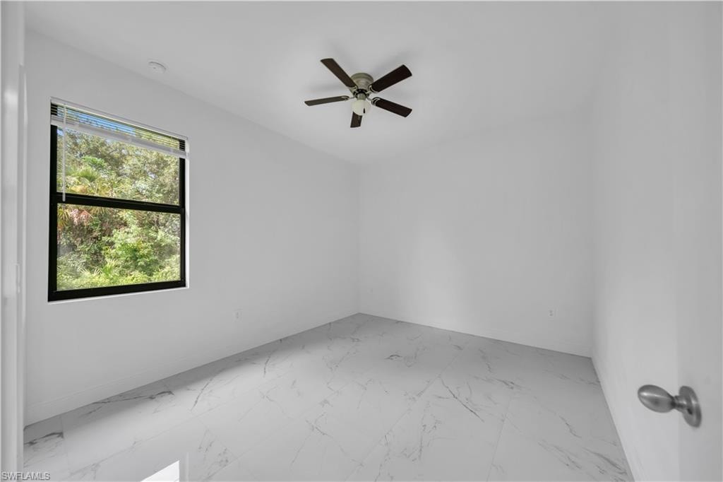 Bright room featuring white walls, large window, ceiling fan, and light-toned marble-look tile flooring