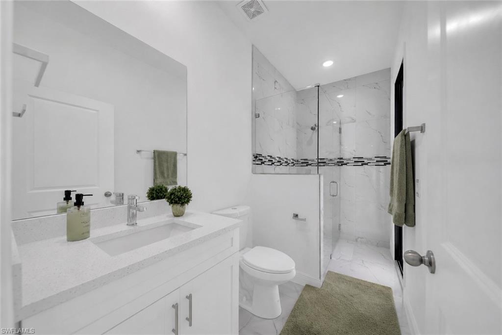 Spa-inspired master bathroom featuring a frameless glass-enclosed walk-in shower with subway tile surround and decorative tile accent band, a white vanity with dual-sink configuration and quartz countertop, white cabinetry with brushed nickel hardware, recessed ceiling lighting, and neutral tile flooring