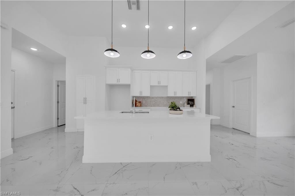 Open-concept kitchen featuring a large central island with a solid surface countertop, white cabinetry, a tiled backsplash, and recessed lighting