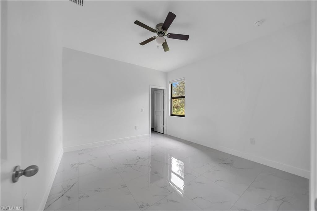 Spacious interior with white walls, large format tile flooring, and a ceiling fan