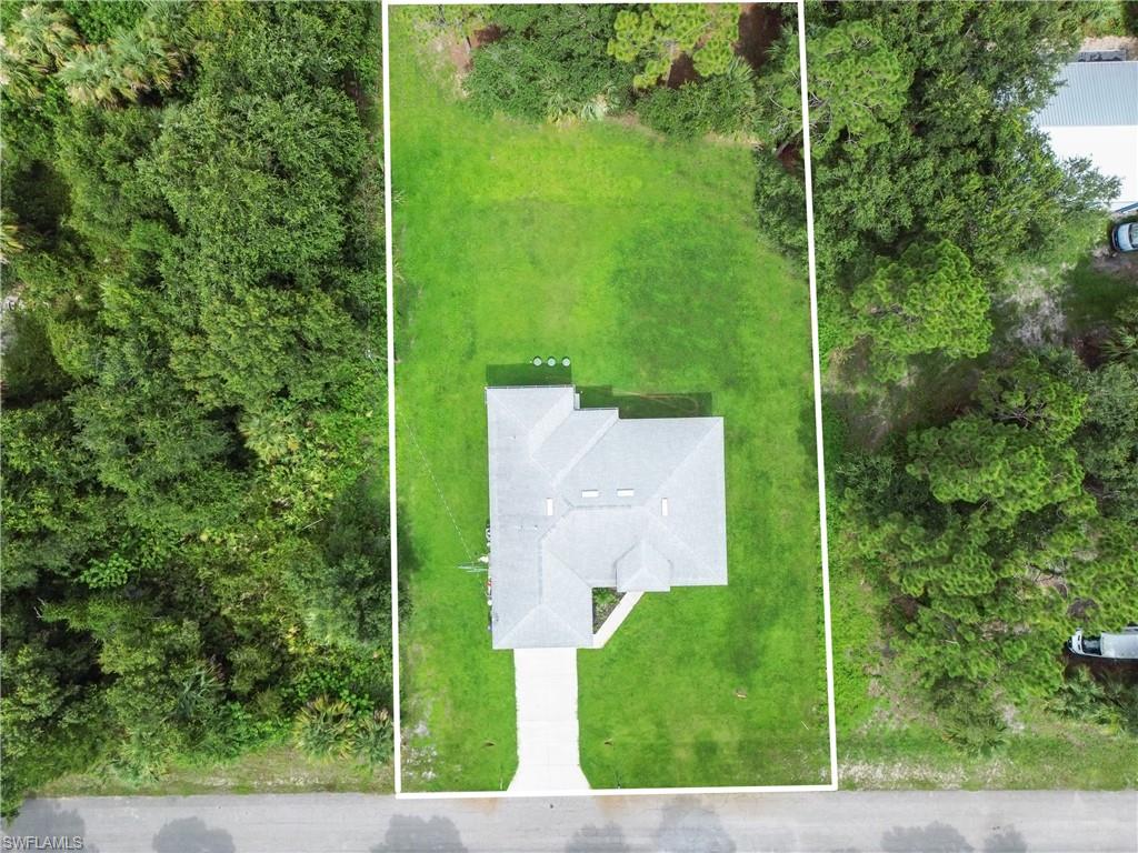 Expansive lot featuring a single-story residence with a gray shingle roof, a verdant lawn, and mature trees bordering the property
