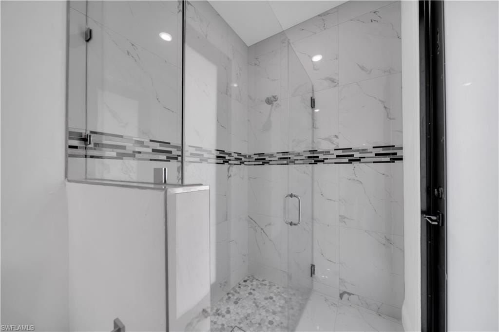 Glass-enclosed shower featuring large format wall tile with a linear mosaic accent, pebble-style floor, and ceiling-mounted recessed lighting