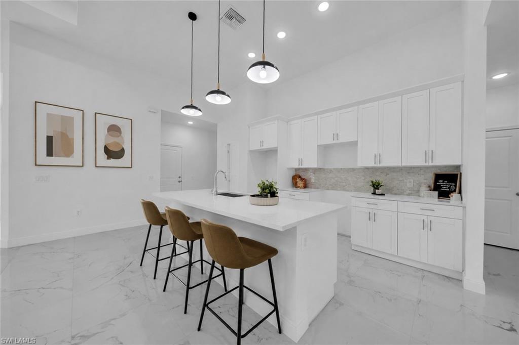 Modern kitchen featuring white cabinetry with brushed nickel hardware, a waterfall-edge white quartz island with seating for three, stainless steel appliances, and gray tile flooring