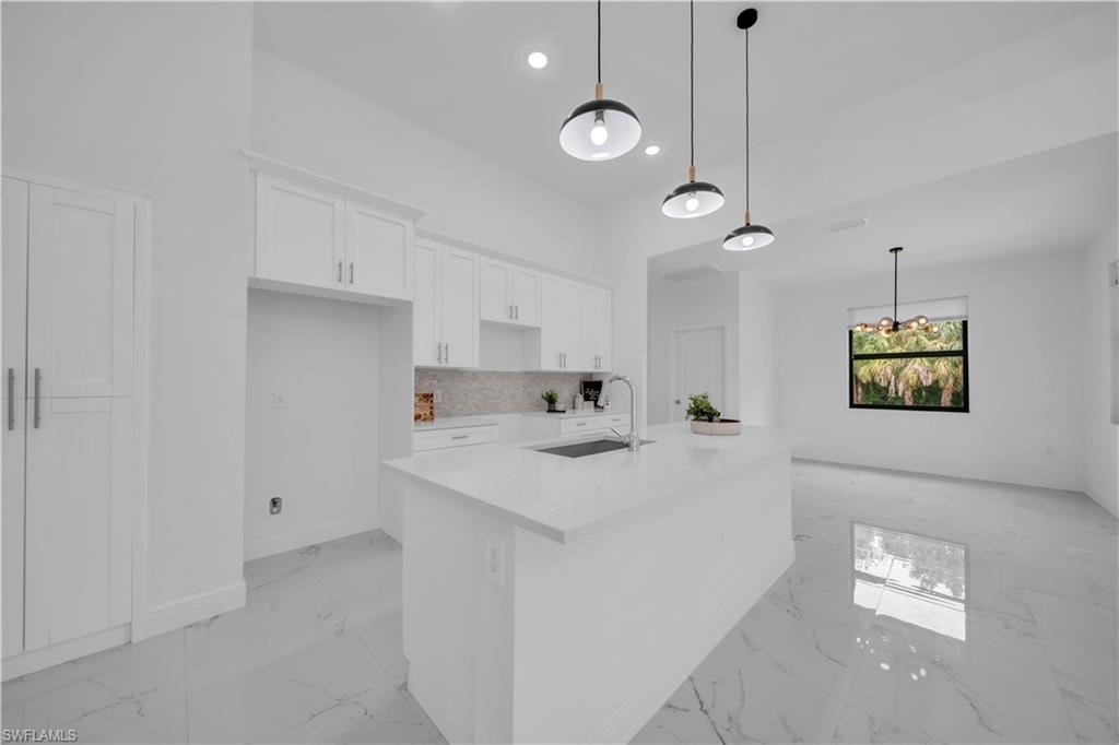 Modern kitchen featuring a large central island with an undermount sink, white cabinetry, and light-toned countertops