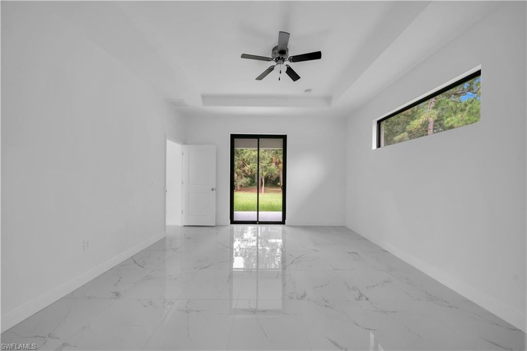 Spacious interior room featuring large format tile flooring, a tray ceiling, and a contemporary ceiling fan