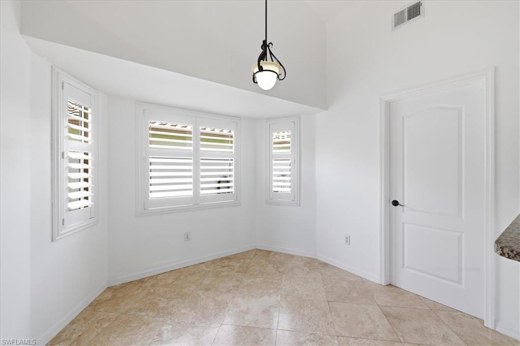 Bay window with white plantation shutters, vaulted ceiling, tile flooring, and a paneled interior door