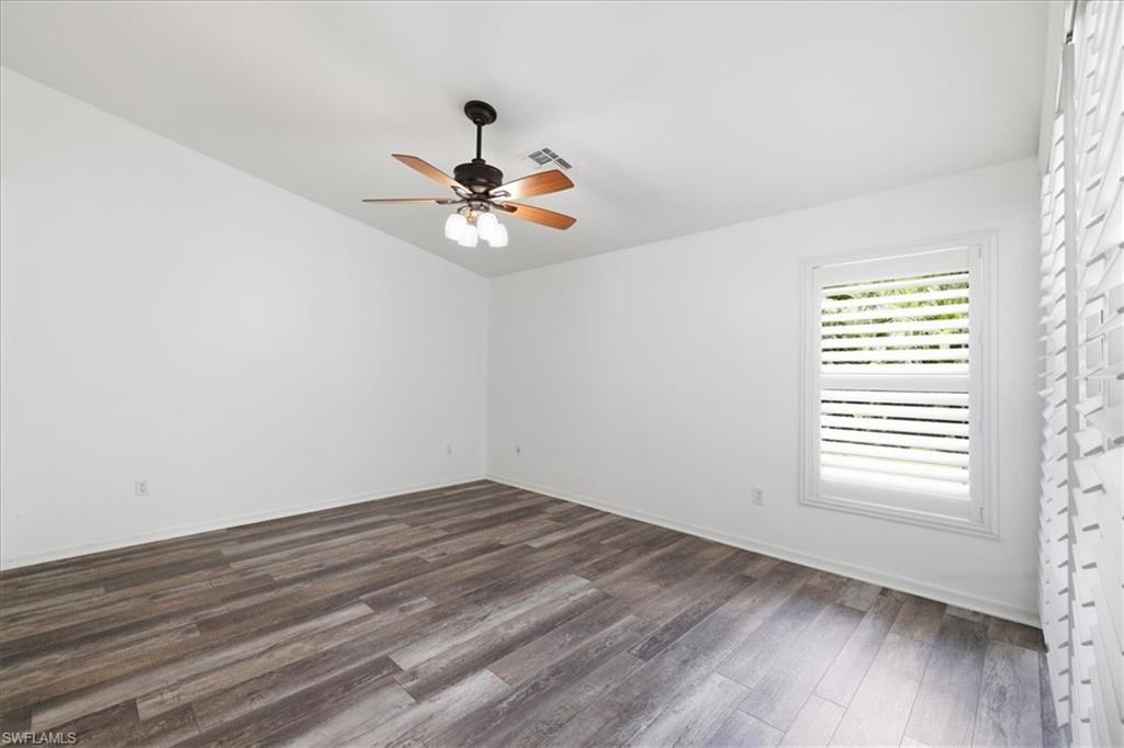 Spacious room featuring wood-finish flooring, a ceiling fan with integrated lighting, and a window with plantation shutters
