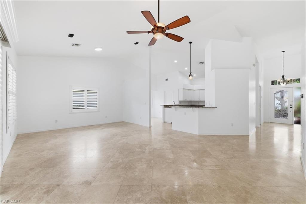 Spacious living area featuring light-toned tile flooring, high vaulted ceilings, and white plantation shutters