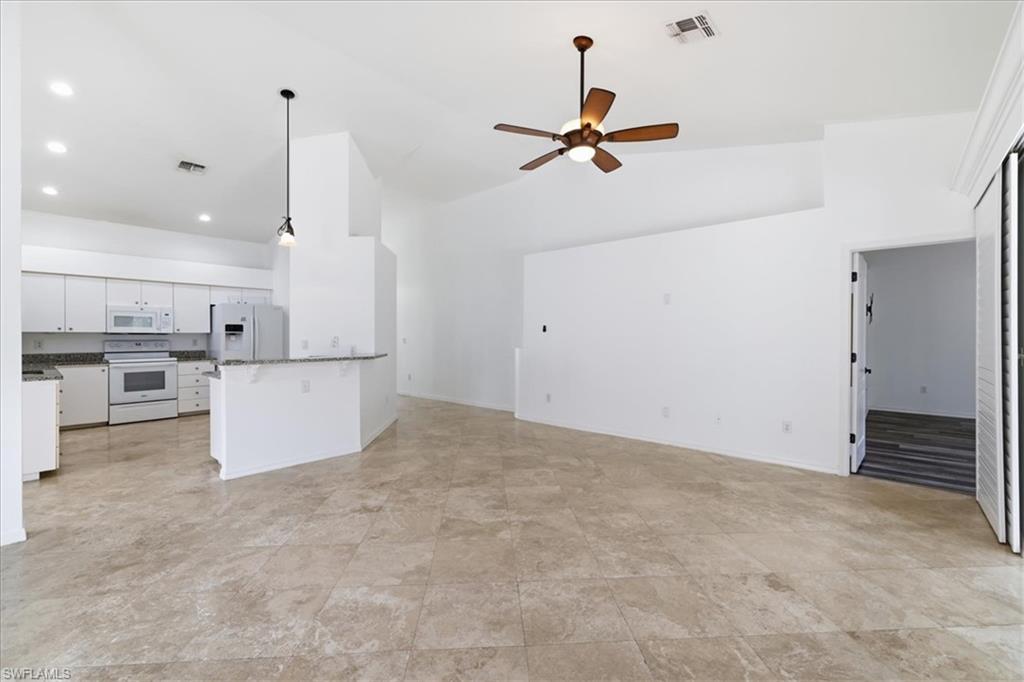 Spacious living area featuring large format tile flooring, vaulted ceilings, and a ceiling fan